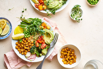 Healthy vegetarian lunch bowl with avocado, chickpeas, quinoa and vegetables, garnished with microgreens and nut dressing. Flat lay on stone background.