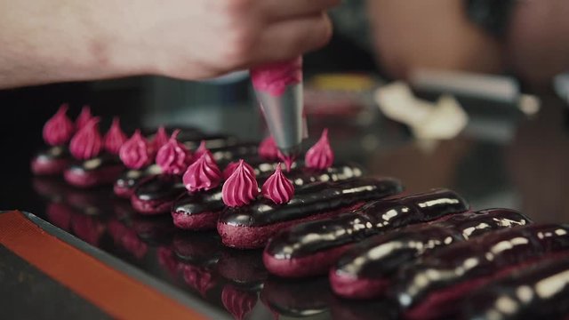 Eclairs or profiterole with chocolate and whipped cream preparing on baking sheet. Spreading chocolate on top of eclair with spoon. Traditional French dessert. 