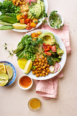 Healthy vegetarian lunch bowl with avocado, chickpeas, quinoa and vegetables, garnished with microgreens and nut dressing. Flat lay on stone background.