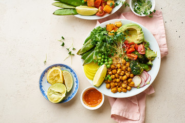 Healthy vegetarian lunch bowl with avocado, chickpeas, quinoa and vegetables, garnished with microgreens and nut dressing. Flat lay on stone background.
