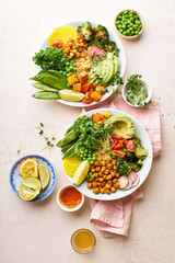 Healthy vegetarian lunch bowl with avocado, chickpeas, quinoa and vegetables, garnished with microgreens and nut dressing. Flat lay on stone background.