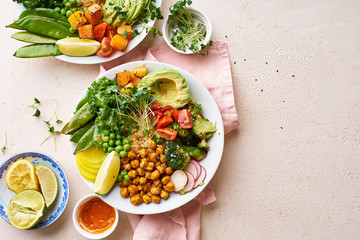 Healthy vegetarian lunch bowl with avocado, chickpeas, quinoa and vegetables, garnished with microgreens and nut dressing. Flat lay on stone background.