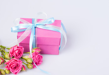 Pink gift box with blue-white ribbon bow and bouquet of red roses on white background