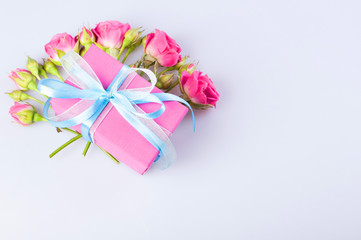 Pink gift box with blue-white ribbon bow and bouquet of red roses on white background