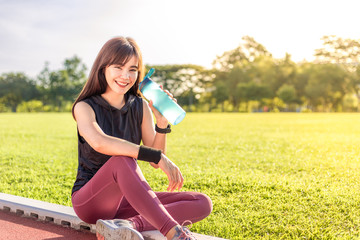 Beautiful young Asian woman exercising in the morning at a running track, taking a rest to drink water