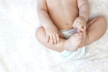Baby boy of 6 months. Boy holds his legs lying on the bed in the bedroom.