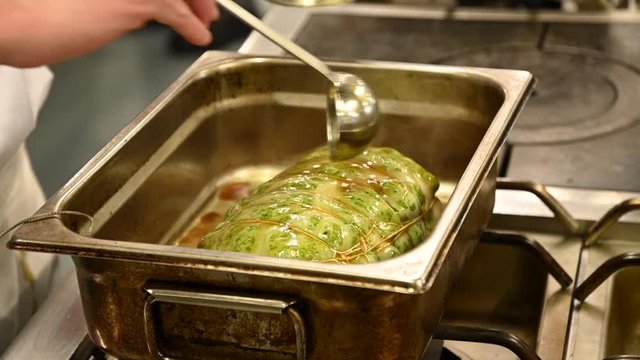 Un chef cuisinier remets de la sauce dans un plat o&ugrave; il y a de la viande ficel&eacute; avec des l&eacute;gumes dans un restaurant