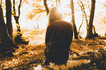 Blonde Frau sitzt mit dem Rücken zum Betrachter auf einem Baumstamm im Wald