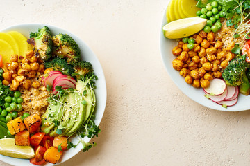 Two bowls of healthy vegetarian lunch with avocado, chickpeas, quinoa and vegetables, garnished with microgreens and nut dressing. Flat lay on stone background, copy space
