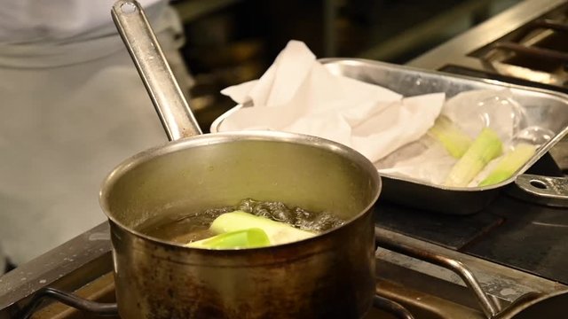 Un chef cuisinier fais cuire des morceaux de poireaux blancs dans une casserole dans un restaurant