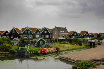 Fototapeta na wymiar Colorful Marken homes with a lawn garden and the canal passing in cloudy weather