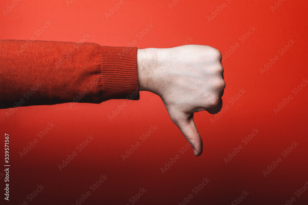 Wall mural Man hand shows thumb down on red background.