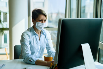 Female entrepreneur with face mask working on computer in the office.