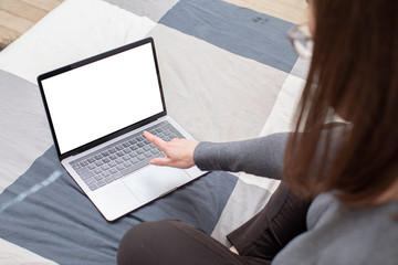 Young woman surfing on her metallic gray laptop and looking for informations on the internet. She has long brown hair, glasses and a gray sweater,  and she sits on a plaid patterned sheet