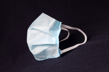 Medical disposable professional mask as a means of personal protection against the virus and bacteria during the spread of the coronavirus influenza pandemic. Respirator in blue on black background.