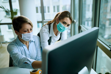 Two businesswomen with face masks working on a computer in the office.
