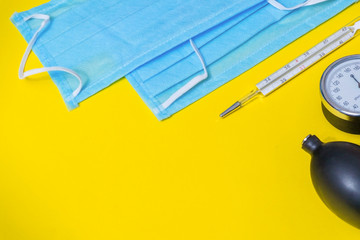 Medical surgical doctor masks, flu and corona virus protection isolated with thermometer and tonometer on yellow background. Health care concept. Copy space for text.