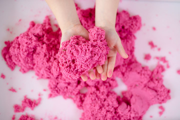Pink magic sand in a kids hands on a white background close up. Early sensory education. Preparing for School. Development - obrazy, fototapety, plakaty