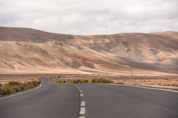 Fototapeta na wymiar An empty road on Fuerteventura countryside, with volcanic mountains in the background