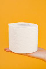 A roll of toilet paper in a woman's hand on a yellow background