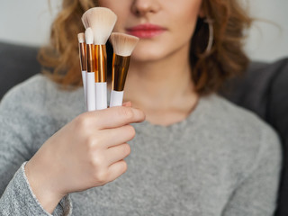 Woman's beauty blogger hands holding a bunch of professional hi-end cosmetic brushes with blurred...