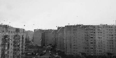 Rainy day city view behind wet window glass. Black and white photography.