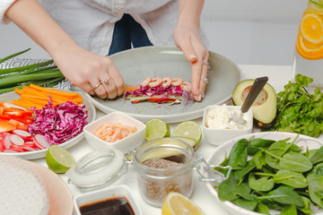 Obraz na płótnie Canvas Woman's hands carefully rolling the spring roll with shrimps. Appetizing shot of asian dish.