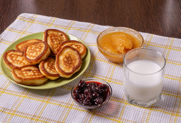Pancakes on a plate, milk in a glass, jam and honey on a napkin on the table.
