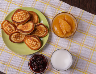 Pancakes on a plate, milk in a glass, jam and honey on a napkin on the table.