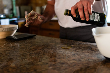Fototapeta na wymiar A man pouring olive oil onto a kitchen worktop in preparation to knead bread dough