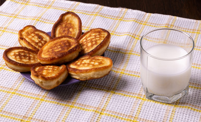 Pancakes in a plate and milk in a glass on a napkin on the table.