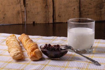 Pastries, milk in a glass and jam on a napkin on the table.