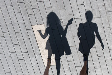 Two women create shadows as they chat and walk along a city street