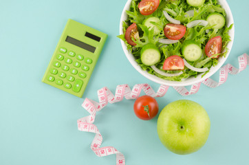 Diet, healthy eating, food and weight loss concept - close up of green apple and measuring tape with salad