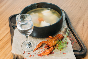 Russian fish soup on a wooden tray in a restaurant, served with boiled crayfish and a glass of vodka