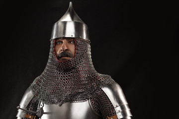 Mannequin man with a beard in a helmet and armor of a knight posing on a black background