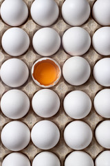 
White raw chicken eggs, top view. One egg is broken, yolk and protein are visible.