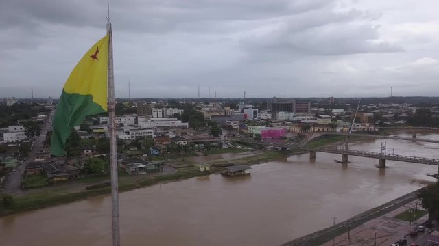 Drone aerial view of Rio Branco city skyline, Acre river, streets, car traffic, bridges, buildings and Acre state flag waving in the wind on a cloudy day on Amazon, Brazil. Concept of architecture. 4K