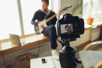 Caucasian musician playing guitar during online concert at home isolated and quarantined. Using camera, laptop, streaming, recording courses. Concept of art, support, music, hobby, education.