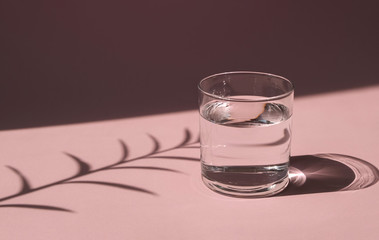 A glass of water lit by the bright sun. Transparent vessel with liquid  on a pink background. Hard shadows.