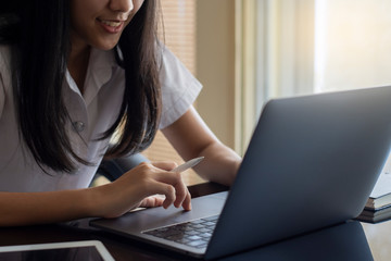 Young happy smiling female asian student working on laptop computer with digital tablet computer pc on the desk at workplace. Online learning concept.