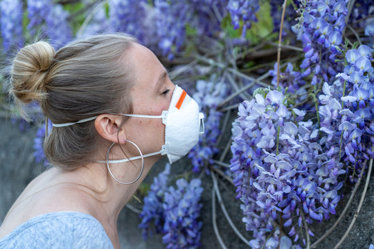 Blonde French Woman Smelling Flowers While Wearing Mask