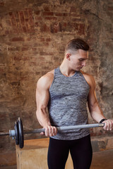 man in a grey sports T-shirt stay against a brick wall .holding a dumbbell