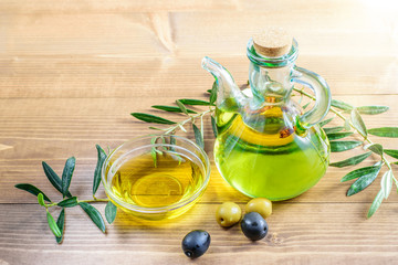 Olive oil bottle with some olives and olive tree branches on the wooden table in sunlights. Healthy food concept.