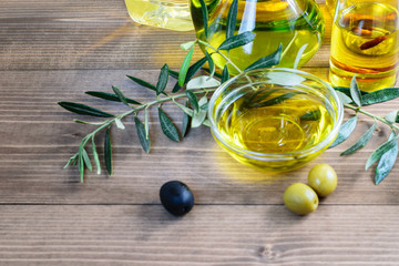 Olive oil in glass transparent bowl and assortment of olive oil bottles on the natural wooden background.