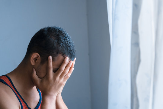Joven hispano cubriendo su rostro con tristeza y llorando dentro de una habitaci&oacute;n.
