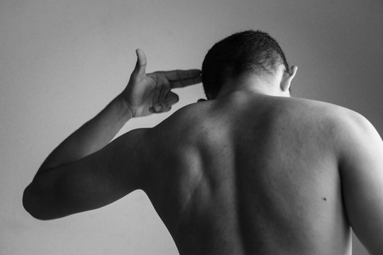 Hombre de espaldas apuntando su mano a su cabeza como una pistola.