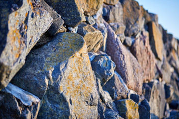 Image of granite coastal stone wall with blue sky in the background. Selective focus.