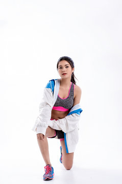 Young beautiful lady wearing sportwear,standing feet apart,kneel down with one knee, put hand touch her leg,stretching body with happy feeling,model posing