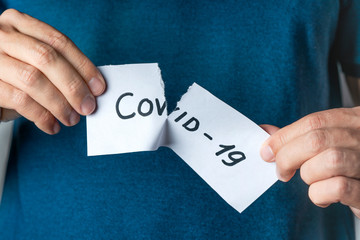 Man tearing card with word COVID-19. End of coronavirus. Victory in fight against Pandemic.